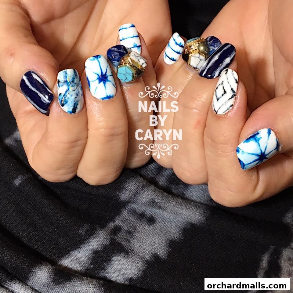 Close-up of hands with intricate blue and white nail art and decorative rings.