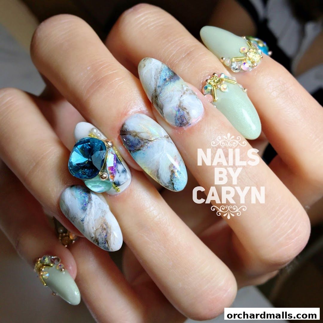Close-up of hands with elaborate marble and jewel-encrusted nail art.