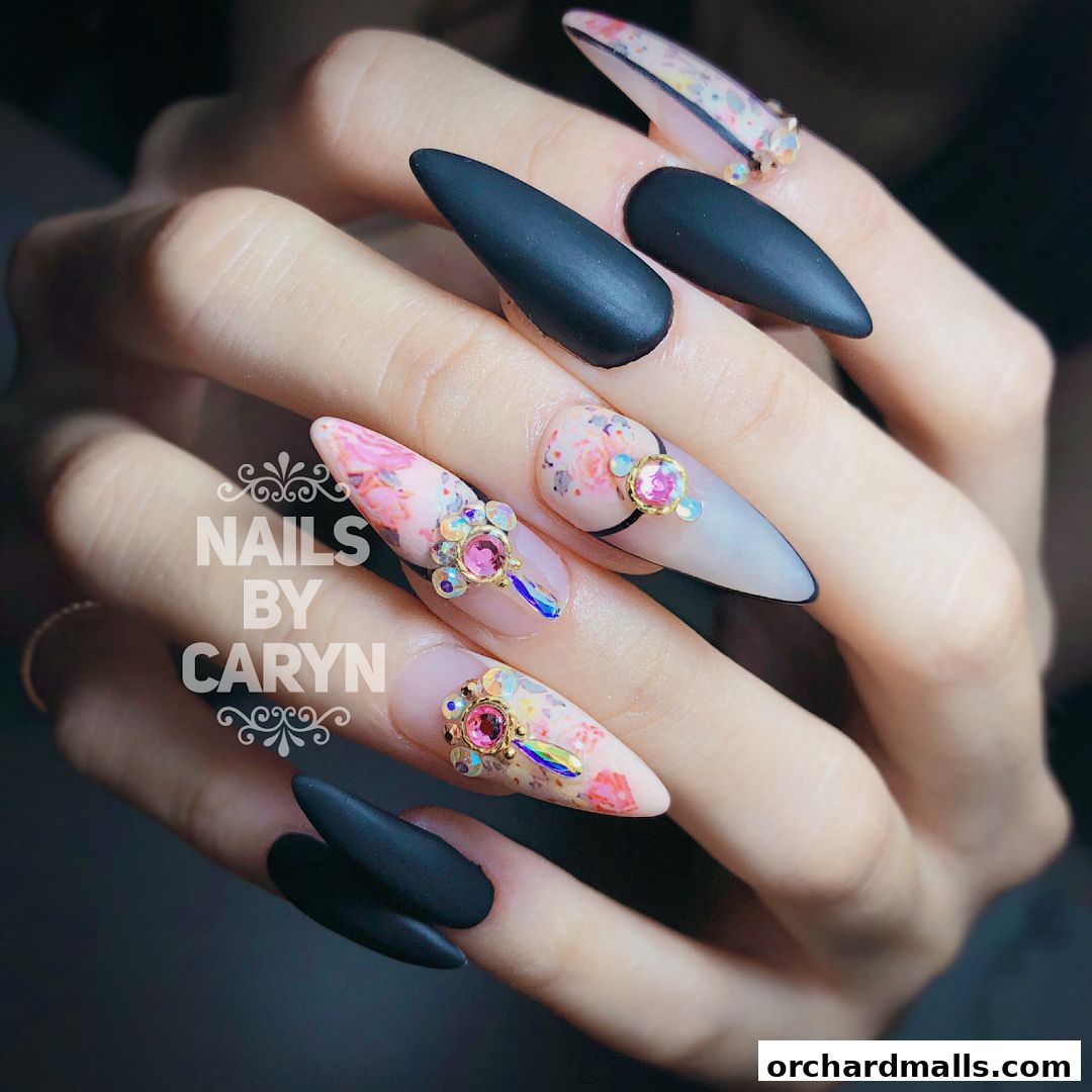 Close-up of a hand showcasing elaborate nail art with matte black and floral designs.