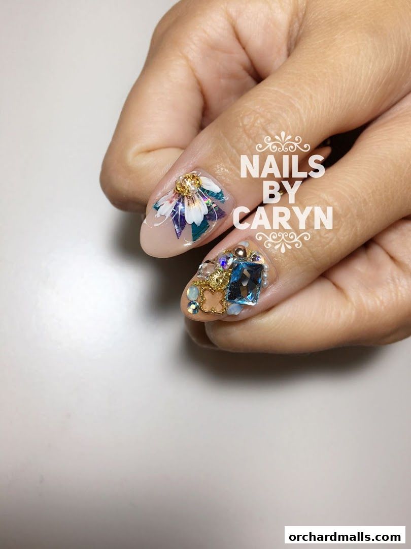 Close-up of a hand with intricately designed nails featuring floral art and gemstones.