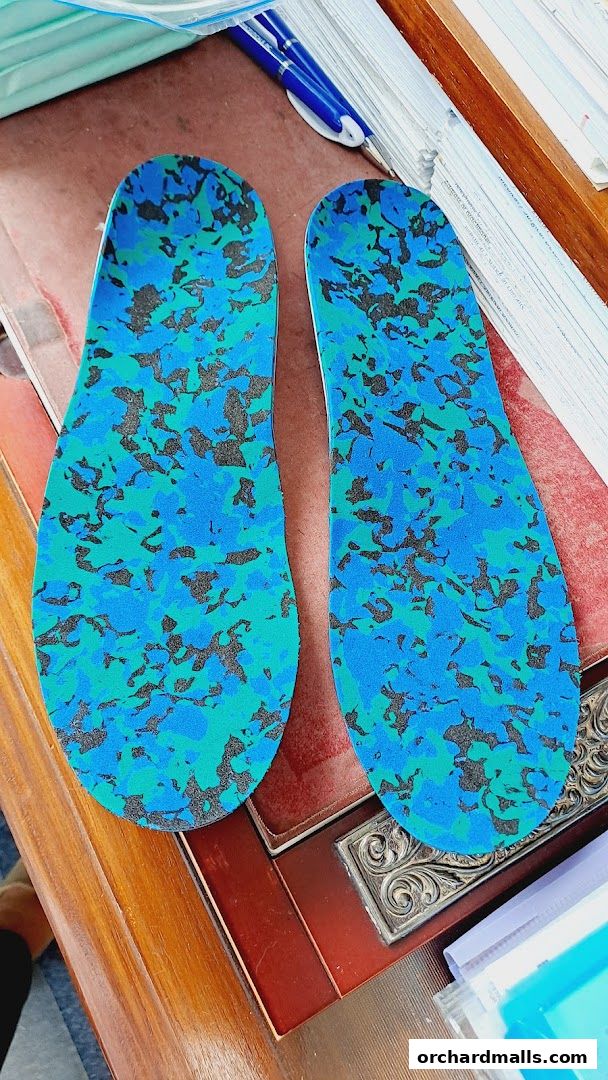 A pair of colorful, patterned shoe insoles are displayed on a wooden surface.