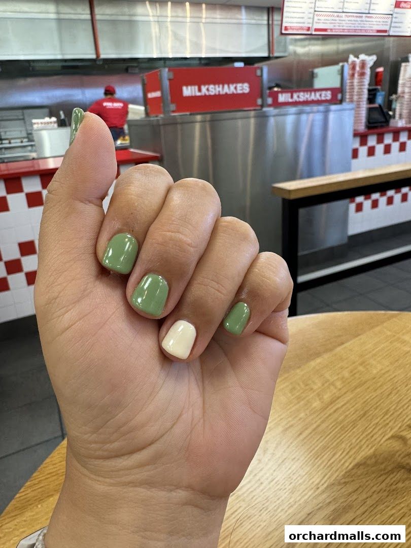 A person's hand with green and white nail polish in front of a restaurant counter.
