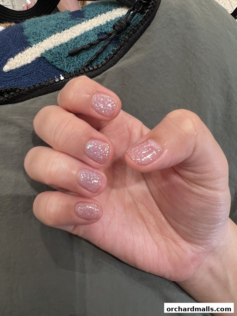 A close-up of a hand with short, glittery pink nails.