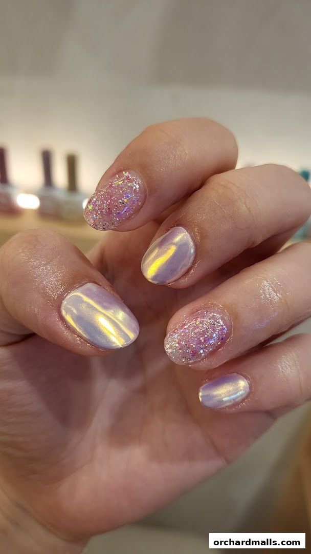 A close-up of a hand with beautifully manicured nails featuring iridescent and glitter finishes.