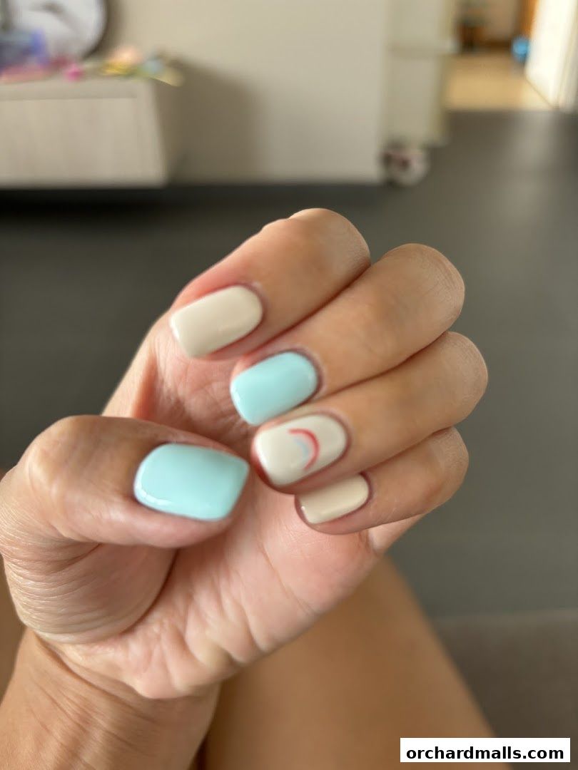 A close-up of a hand with neatly manicured nails in pastel blue and cream colors.