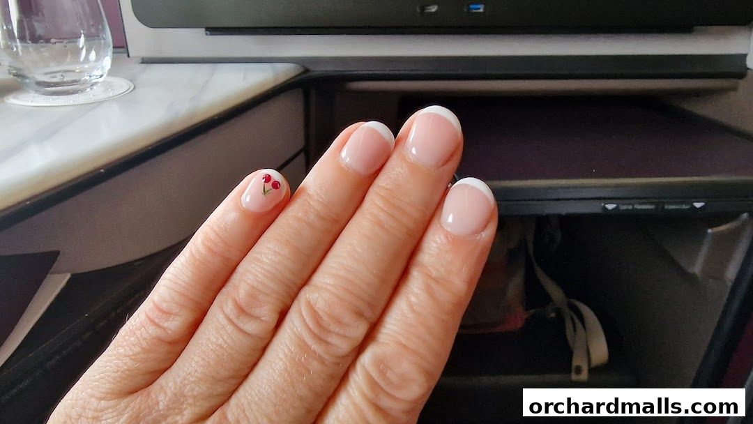 A close-up of a hand with French manicured nails and a small cherry design on one nail.
