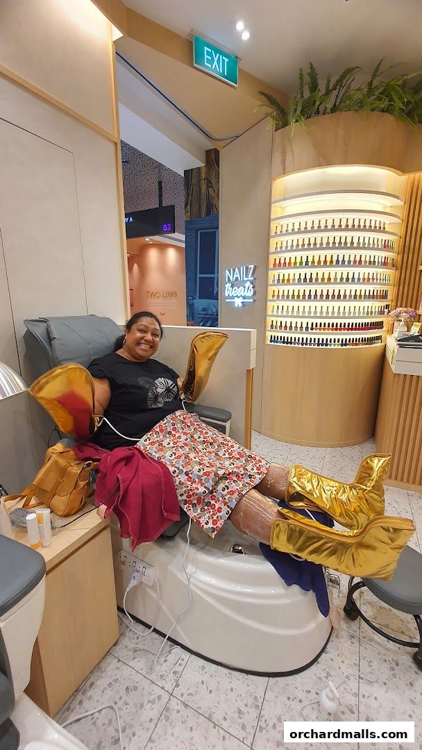 A woman is relaxing in a pedicure chair with gold leg massagers at Nailz Treats.