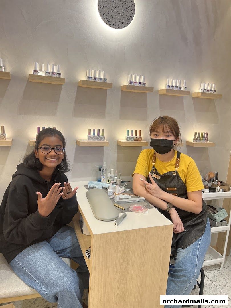 A smiling customer shows off her nails while a nail technician works at a salon.