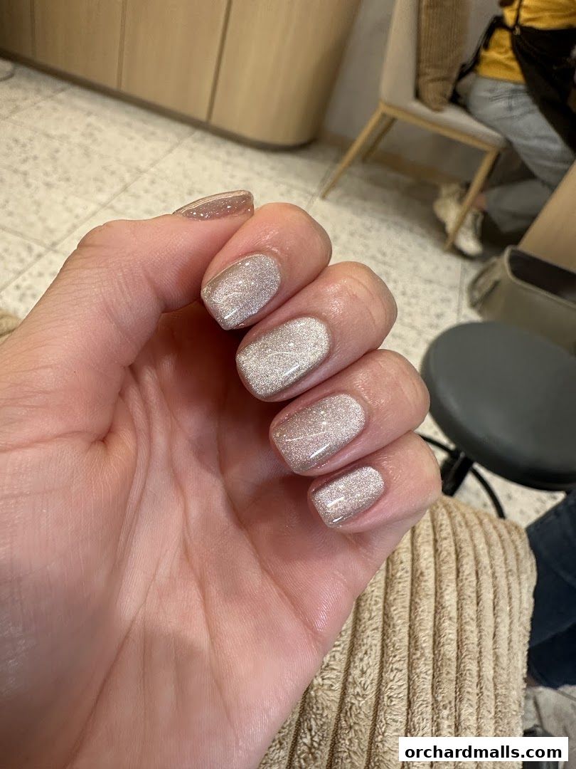 A close-up of a hand with beautifully manicured nails featuring a subtle glitter polish.