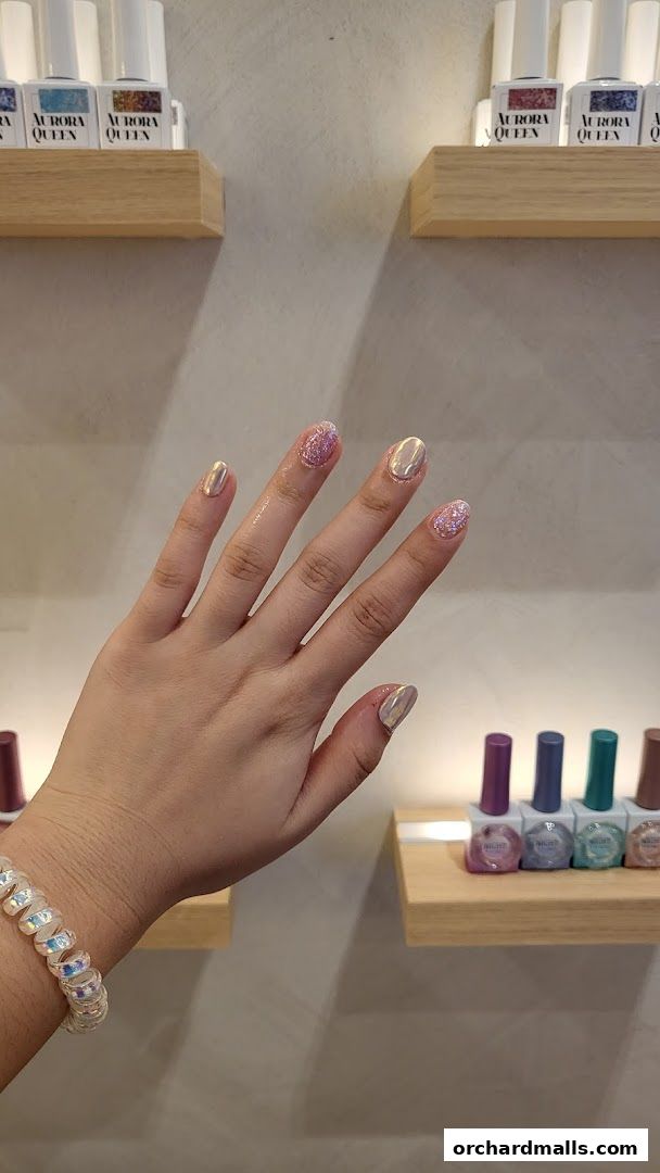 A hand with shimmering holographic and glitter nail polish, with nail polish bottles displayed on shelves.