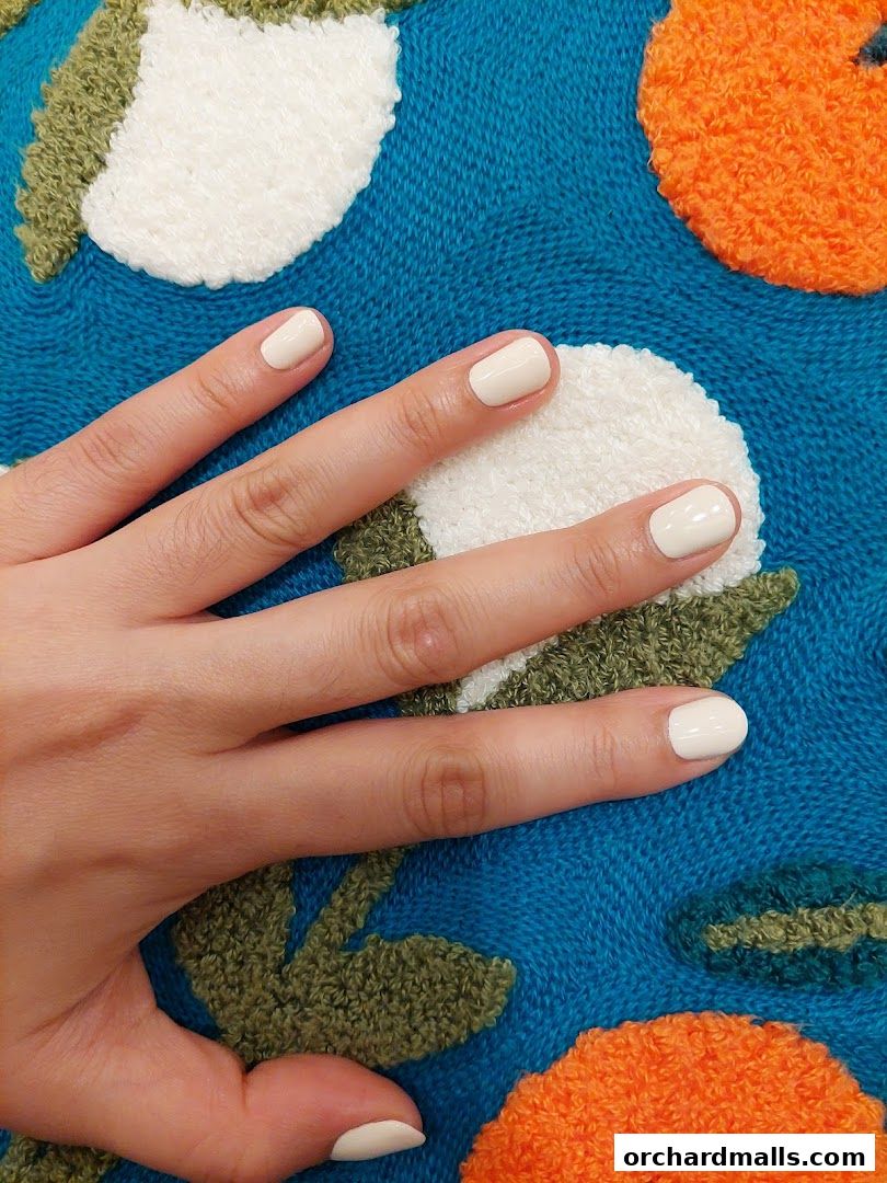 A hand with neatly painted cream-colored nails rests on a textured blue fabric with embroidered floral designs.