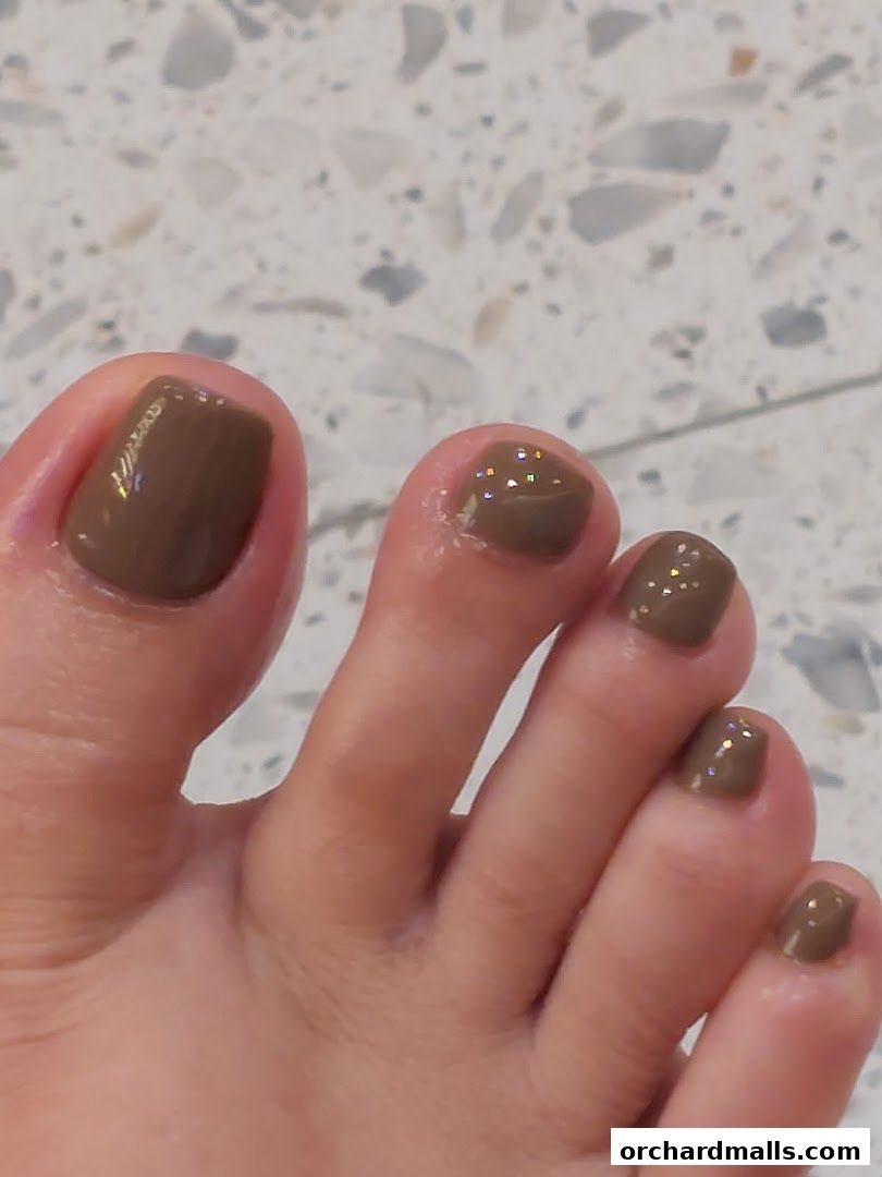 Close-up of toes with polished brown nails and subtle glitter accents.