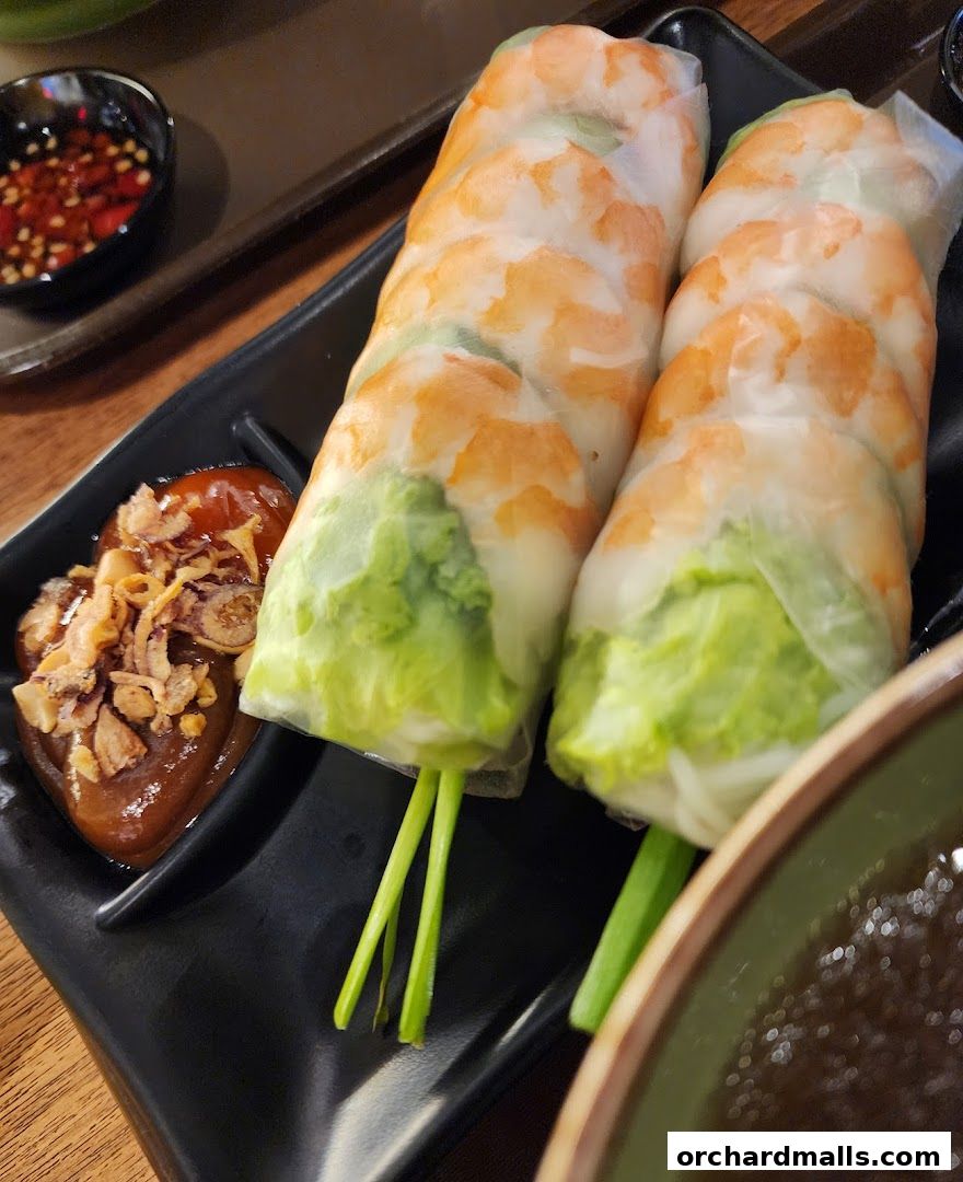 Fresh Vietnamese spring rolls with shrimp, lettuce, and dipping sauce on a black plate.