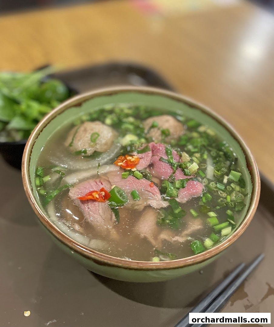 A steaming bowl of beef pho with fresh herbs and chili, served with chopsticks.