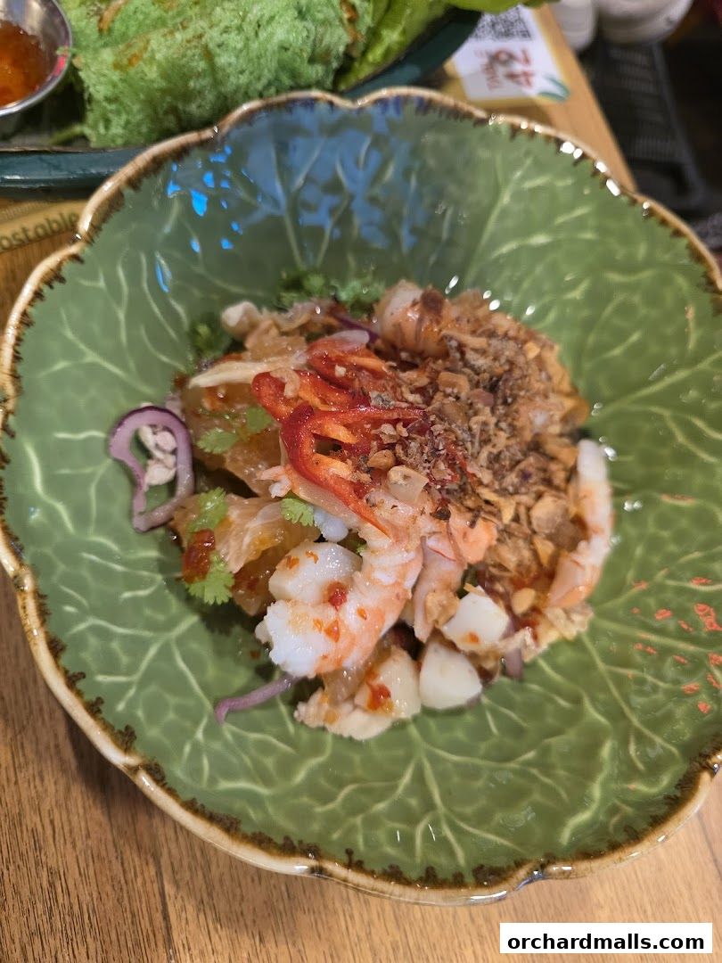 A vibrant salad with shrimp, pomelo, chili, and crispy shallots served in a leaf-shaped bowl.