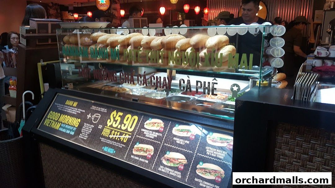 A display case filled with banh mi sandwiches and a menu board with prices.