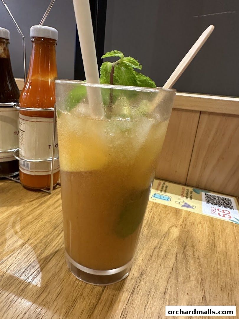 A refreshing iced drink with mint and straws on a wooden table with condiments.