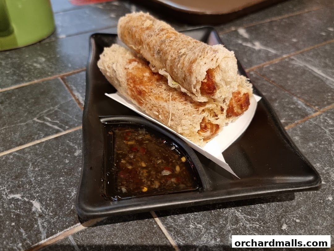 Crispy spring rolls served with a dipping sauce on a black plate.