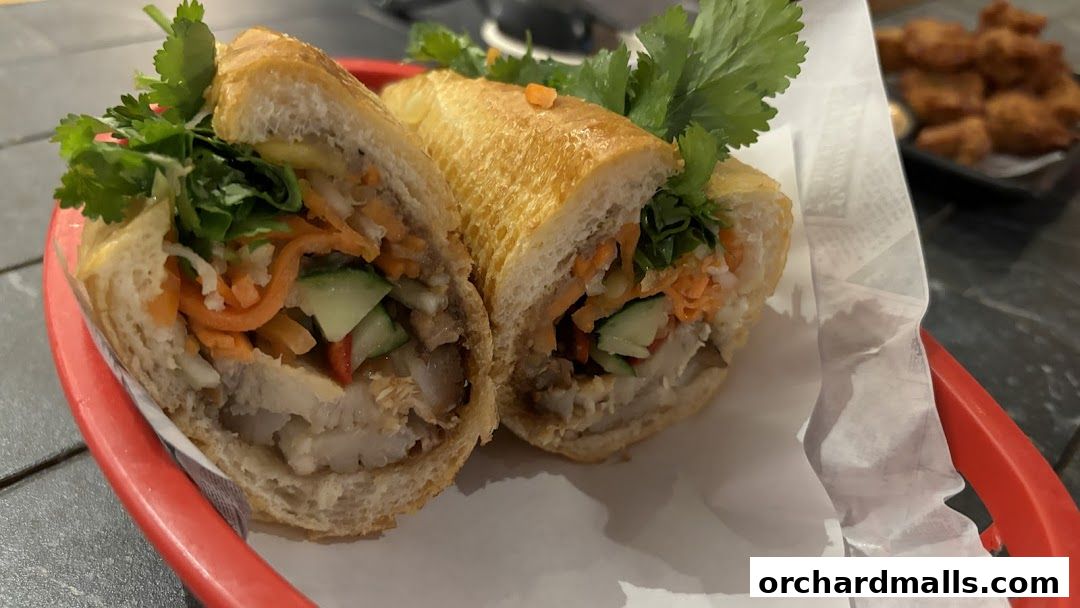 A delicious banh mi sandwich cut in half, served in a red basket with a side of fried items.