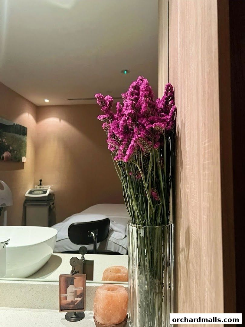A serene spa room with a massage bed, sink, and decorative flowers.