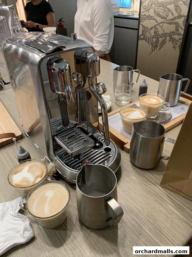 A Nespresso machine with two coffees and milk pitchers on a wooden counter.