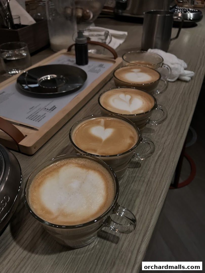 A row of five lattes with latte art, presented on a wooden counter.