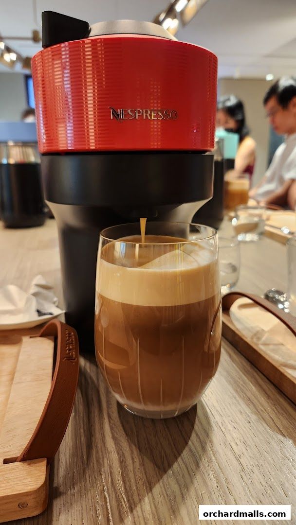 A Nespresso machine brews a coffee into a glass with a thick layer of foam.