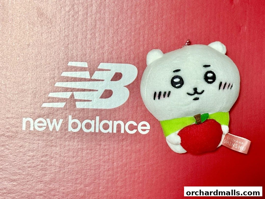 A New Balance logo next to a cute plush toy holding an apple.