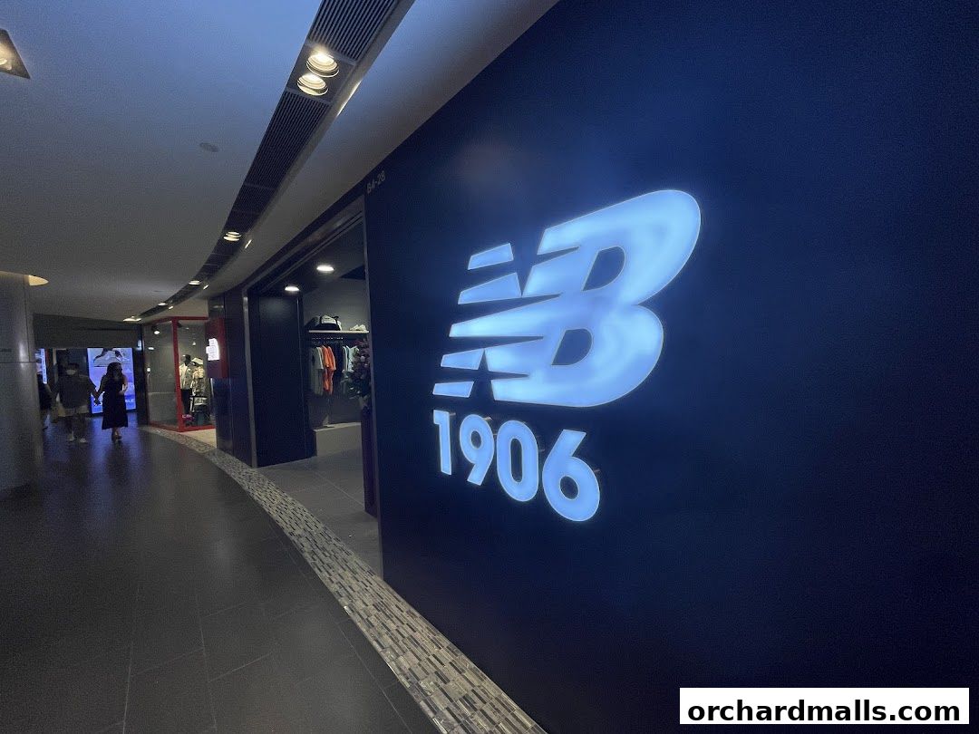 The illuminated New Balance logo and '1906' text on a dark wall, with a shop interior visible.