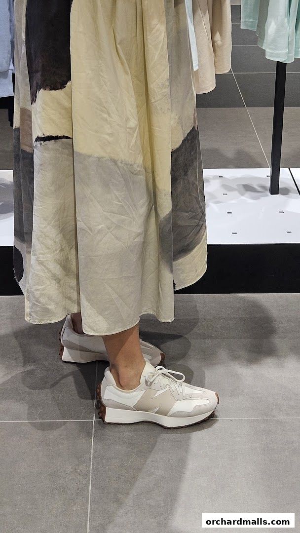 A person wearing New Balance sneakers and a patterned dress inside a store.