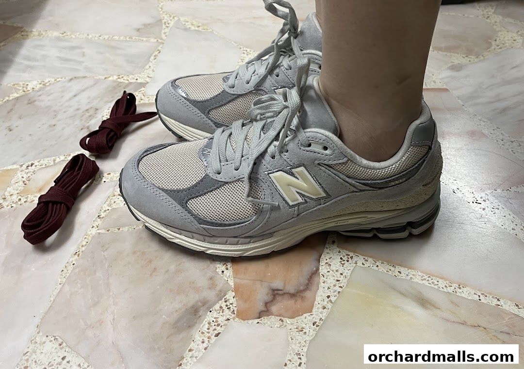 A person wearing light grey New Balance sneakers with maroon laces on the side.