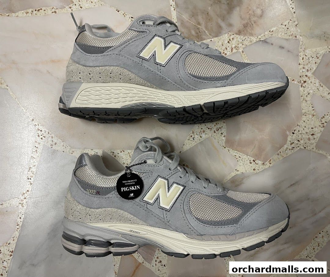 A pair of grey New Balance sneakers with a 'Pig Skin' tag displayed on one shoe.