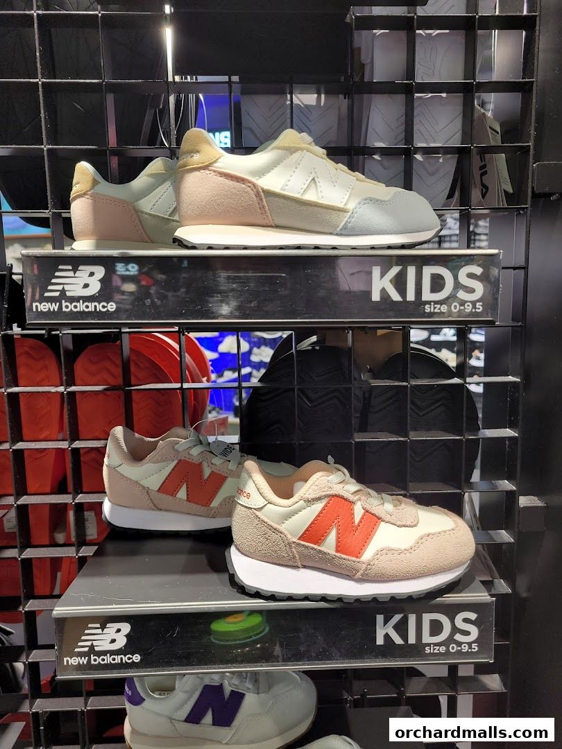New Balance kids' shoes displayed on shelves, featuring pastel and orange colorways.