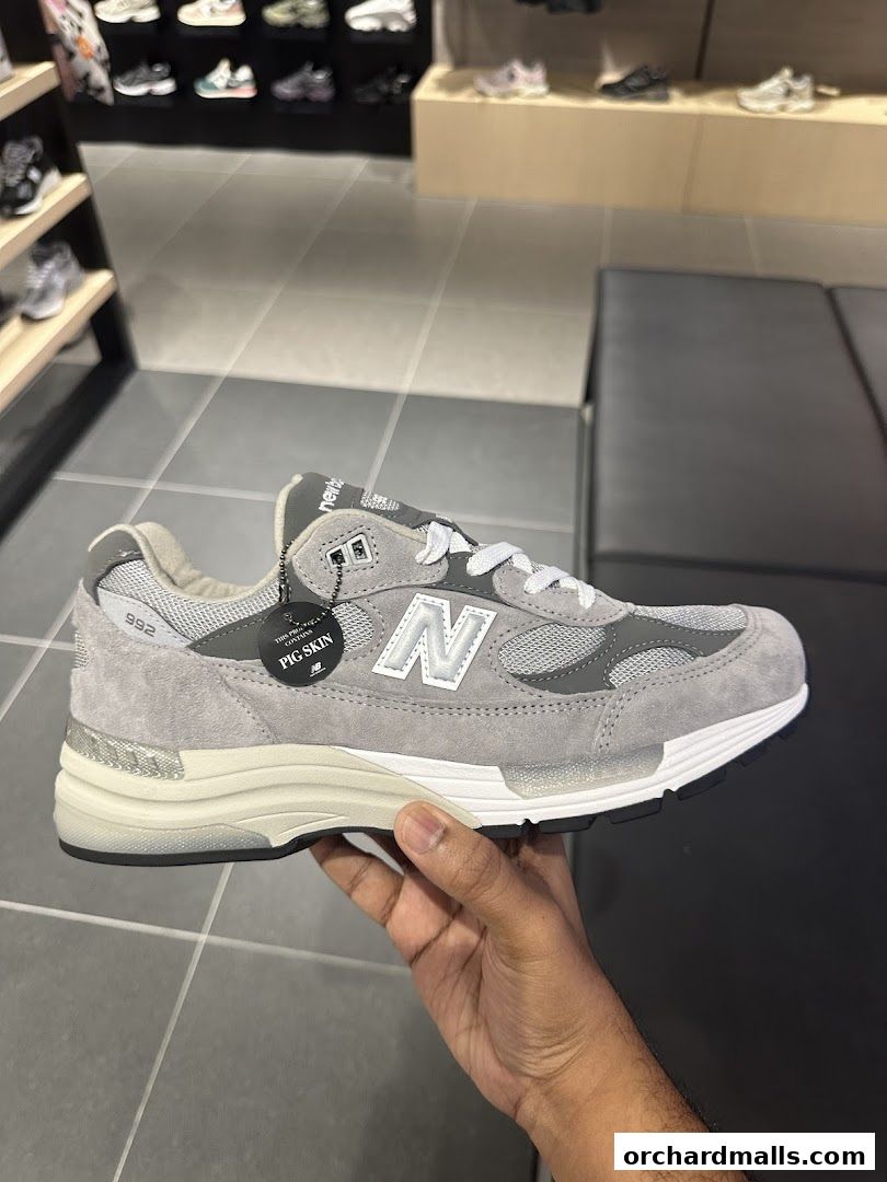 A hand holds a grey New Balance sneaker with a 'Pig Skin' tag.