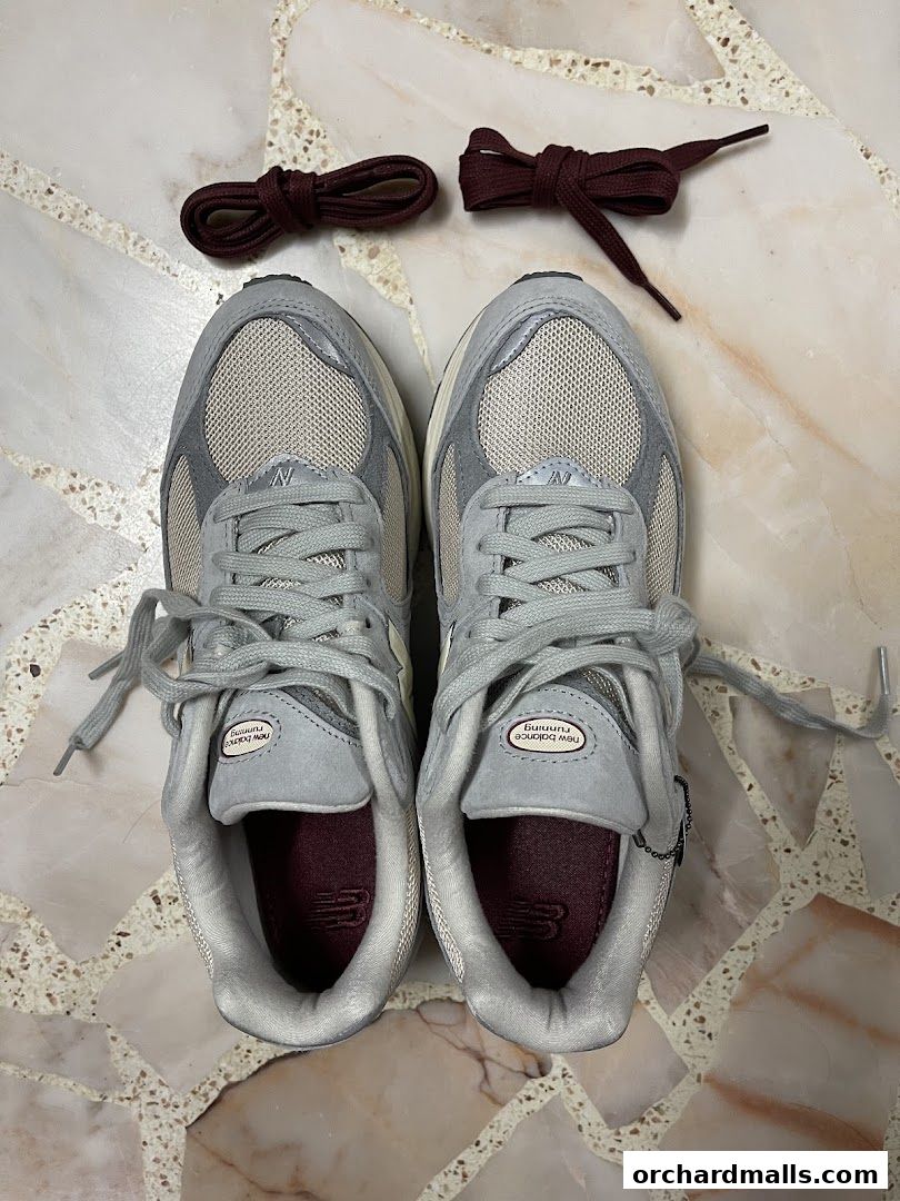 A pair of New Balance sneakers with maroon laces on a speckled floor.