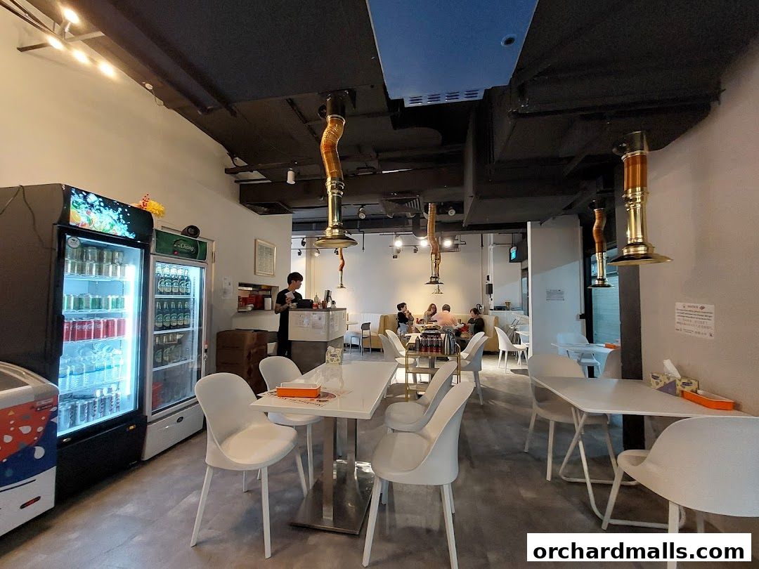 Interior of a modern Thai Mookata restaurant with tables, chairs, and a beverage fridge.