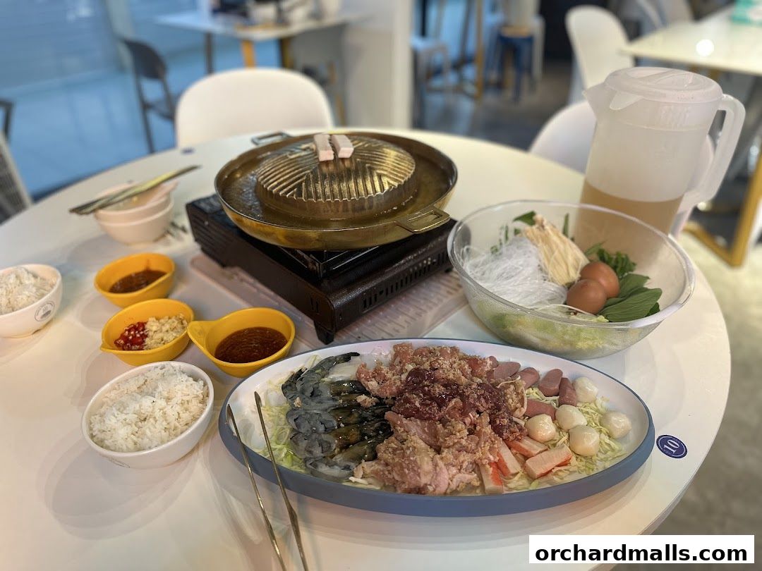A table set for Mookata Thai food with ingredients, rice, sauces, and a grill.