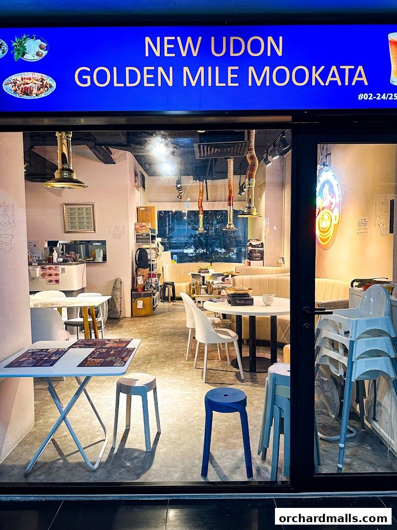 Exterior view of New Udon Golden Mile Mookata Thai Food restaurant with tables and chairs visible inside.