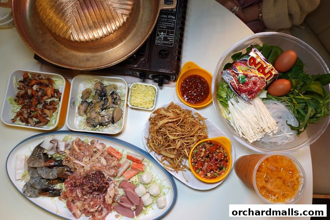 A spread of Mookata ingredients including meats, seafood, vegetables, and dipping sauces.