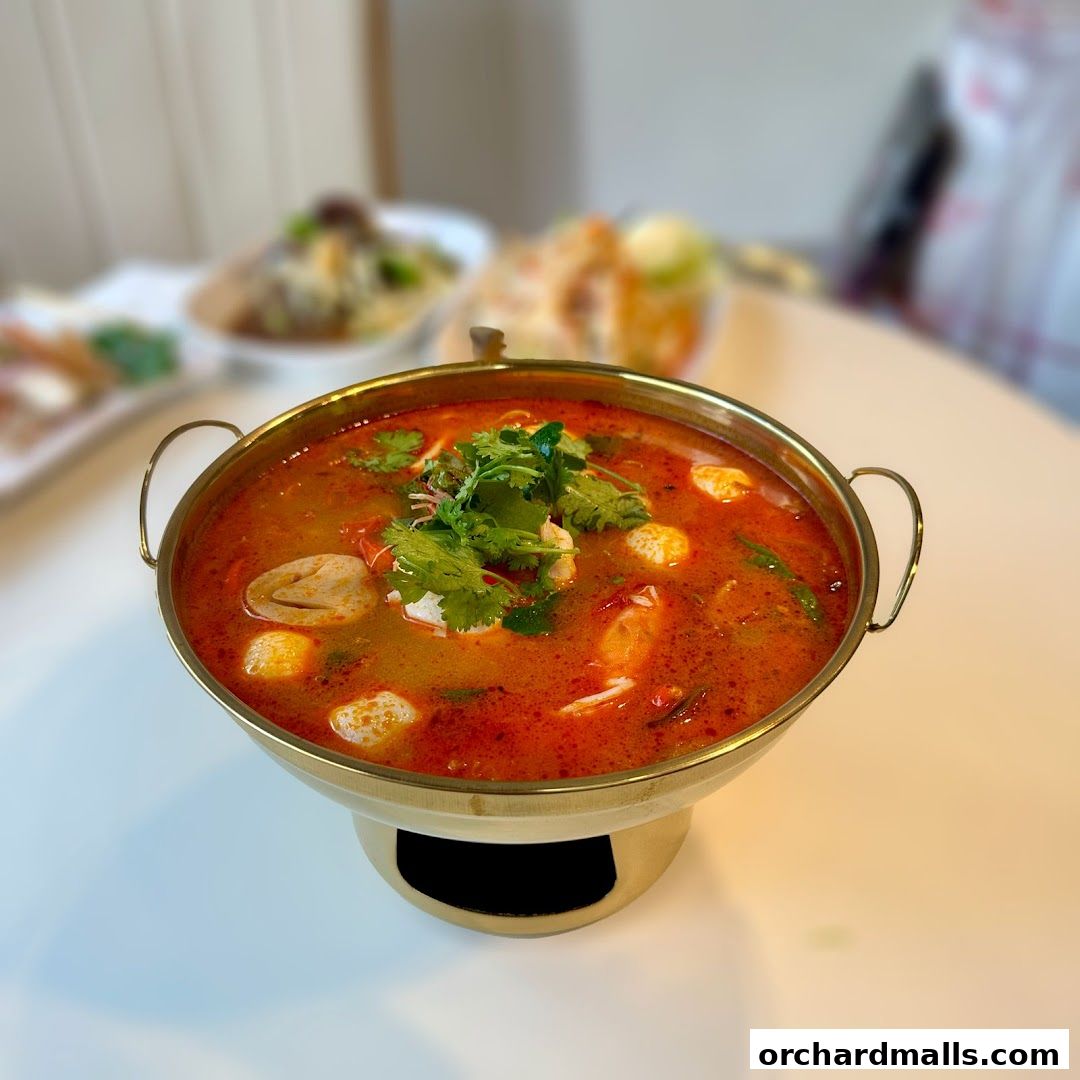 A steaming bowl of Tom Yum soup with shrimp and mushrooms, garnished with cilantro.