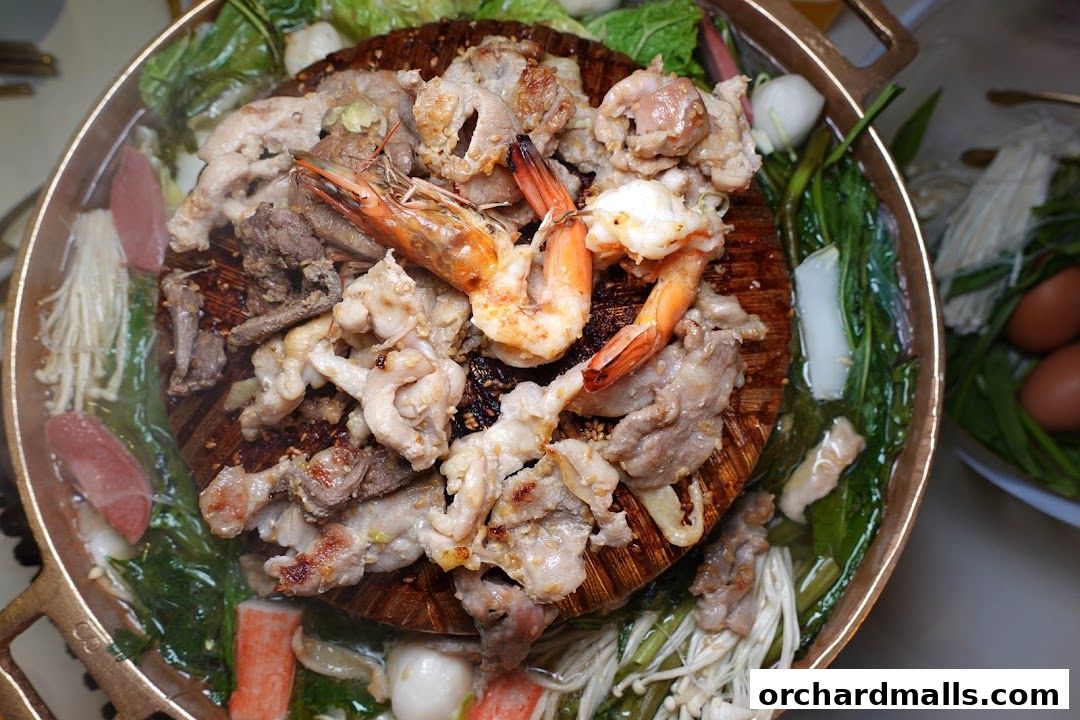A close-up overhead view of a steaming Mookata pot filled with meats, seafood, and vegetables.