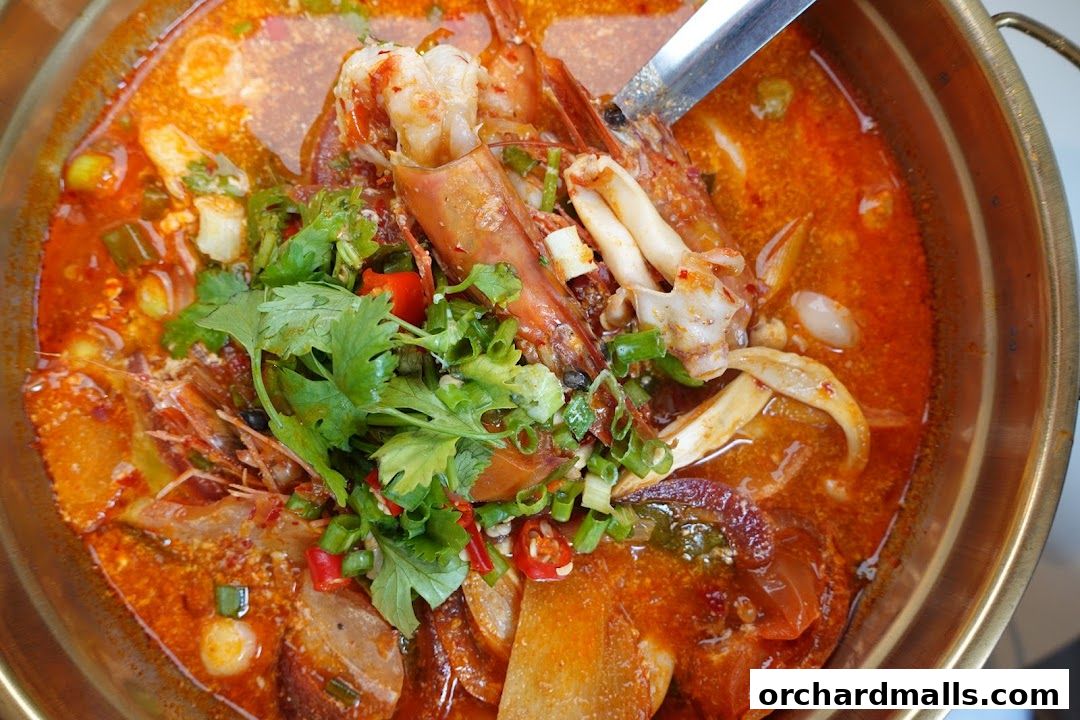 A close-up shot of a steaming bowl of Thai Tom Yum soup with large prawns and fresh herbs.