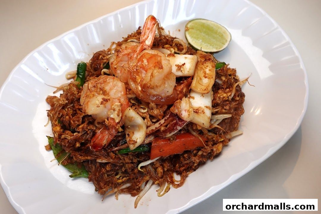 A plate of Thai food with noodles, shrimp, squid, and a lime wedge.
