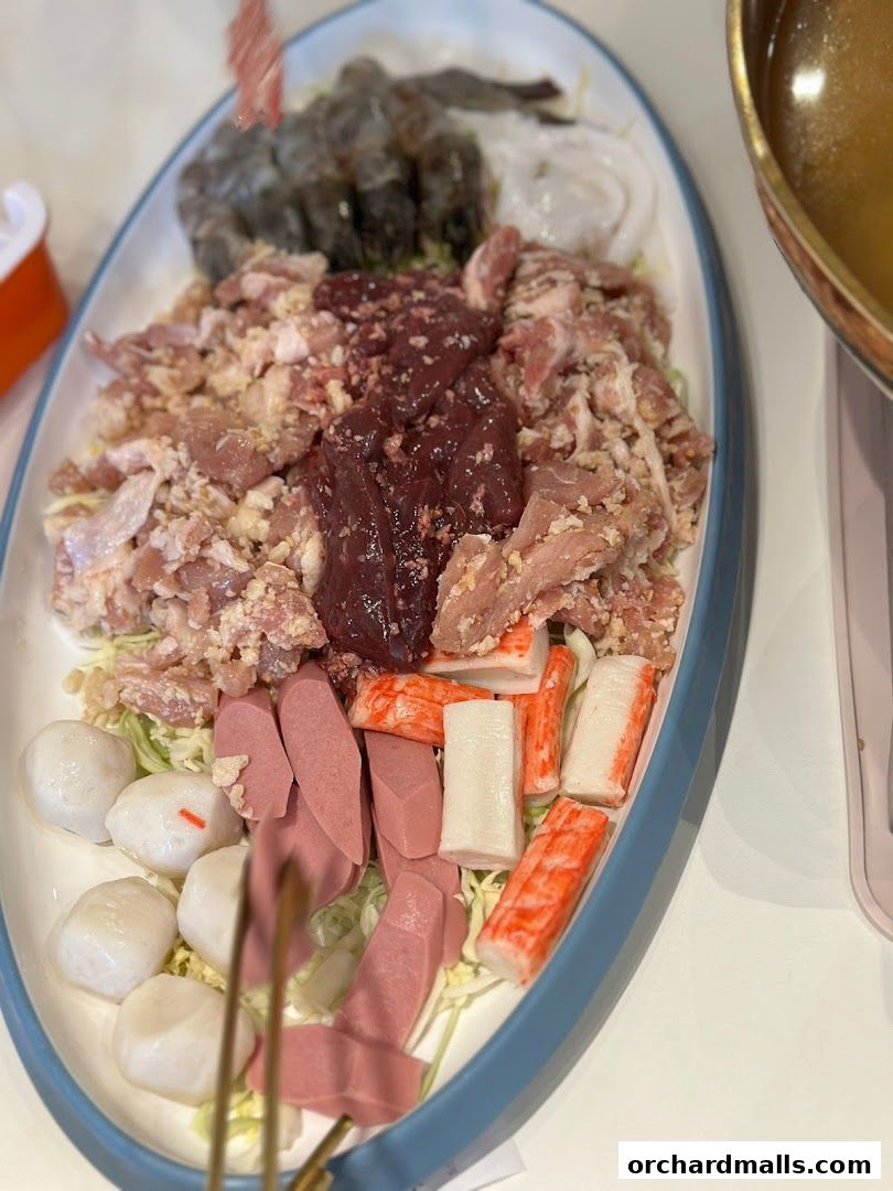 A platter of raw ingredients for Mookata, including meats, seafood, and sausages.