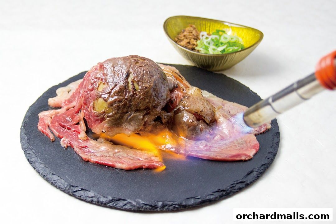 A piece of raw beef is being seared with a blowtorch on a slate plate, with a side dish of chopped green onions.