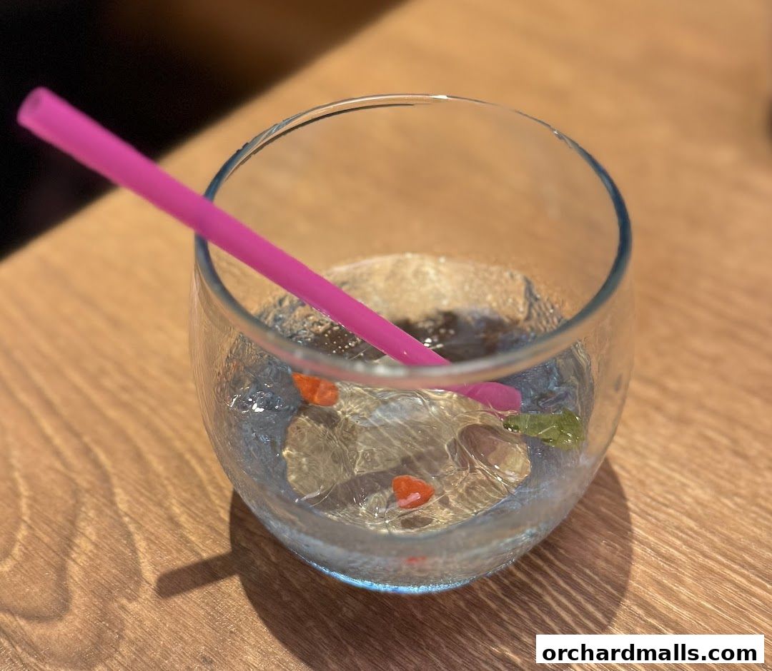 A clear glass with a pink straw and small fruit pieces on a wooden table.