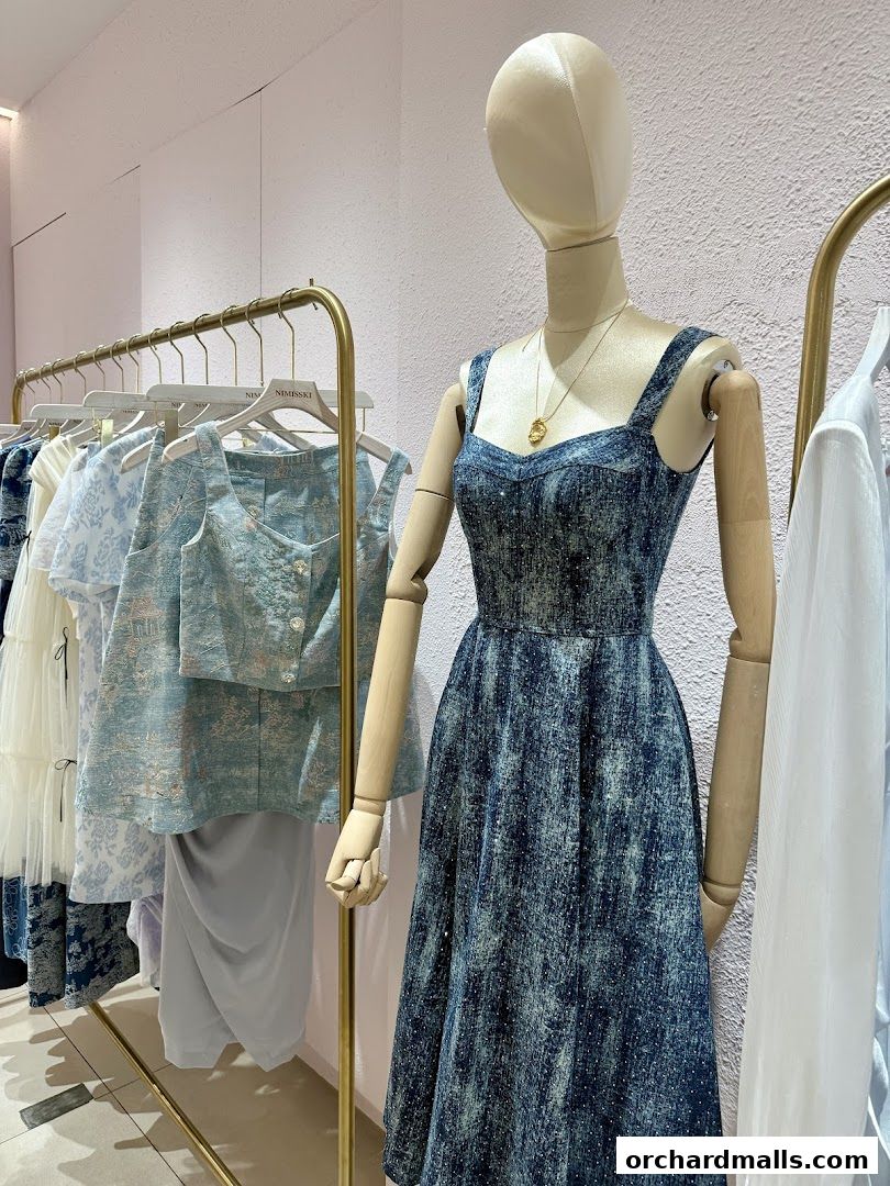 Mannequin displays a blue patterned dress and clothing rack with light blue garments.