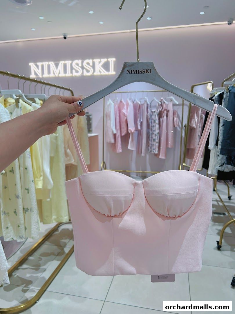 A hand holds a pink bustier top in front of a clothing store display.