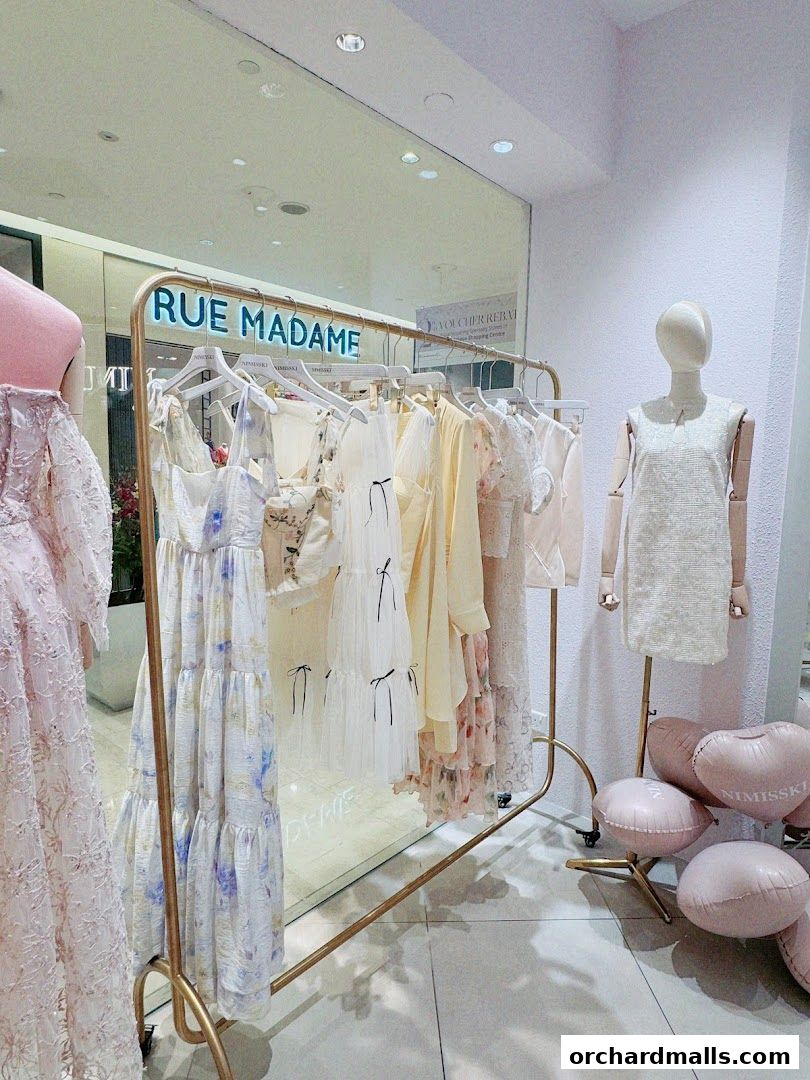 A clothing rack displays elegant dresses, with mannequins and pink balloons in a boutique.