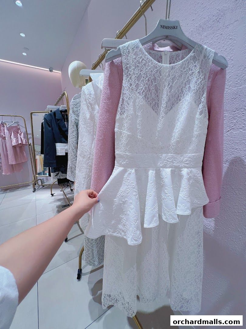 A hand touches a white lace dress on a hanger in a clothing store.
